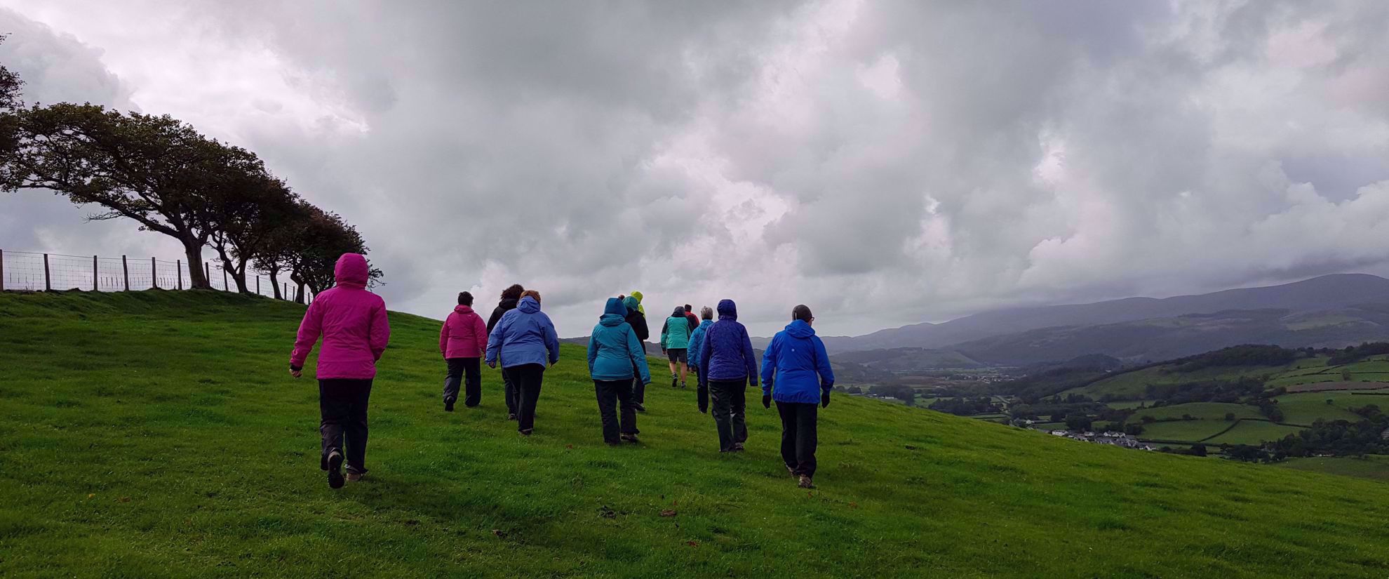 women hiking green hill on cloudy day whales
