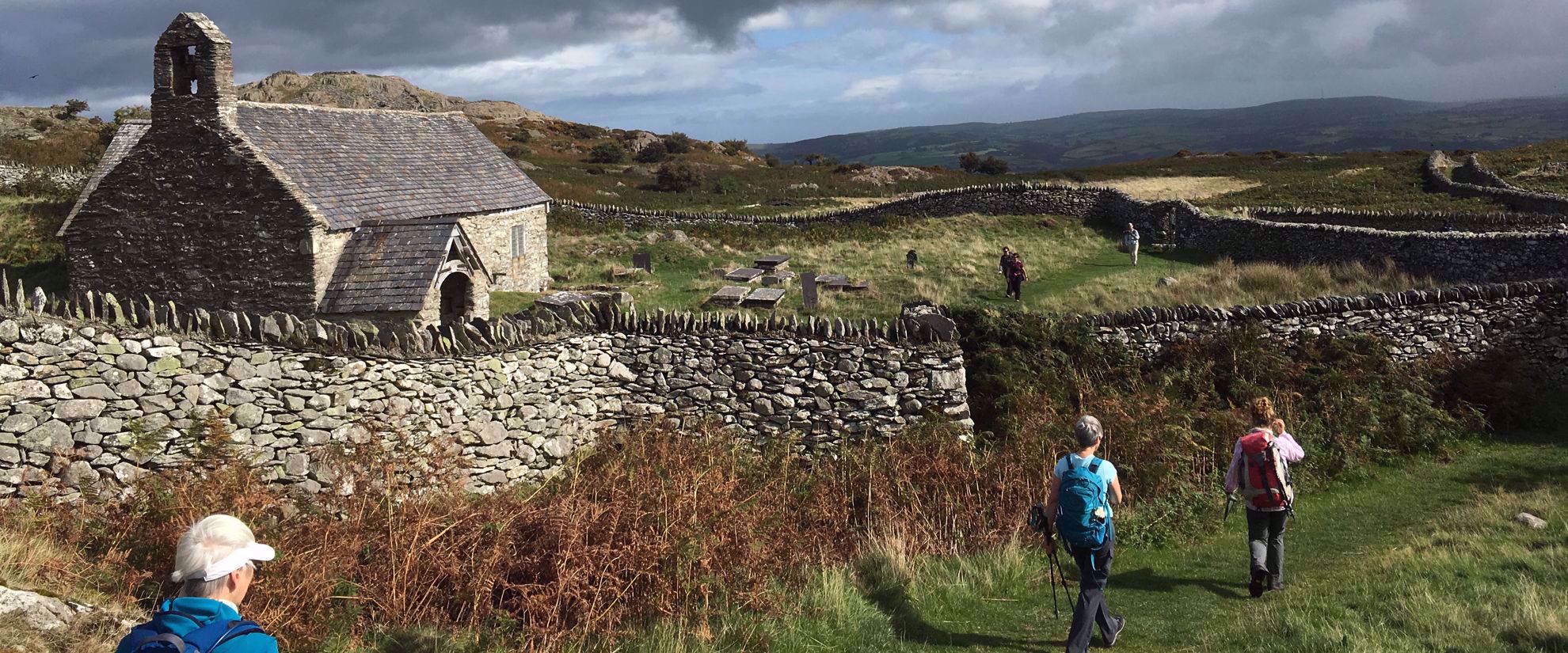 women walking past rock wall and home