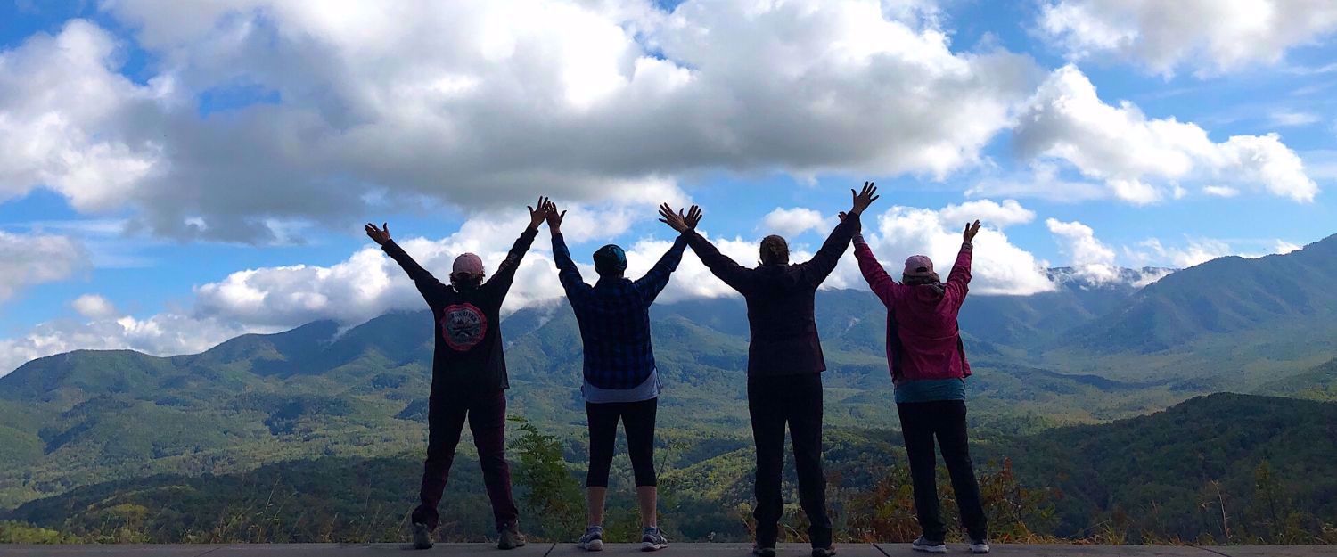 Women standing arms raised blue sky and great smoky mountins in background